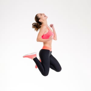 Attractive excited fitness girl in sportwear jumping of joy isolated over white background