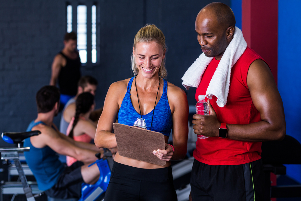 Smiling fitness instructor discussing with man standing in gym
