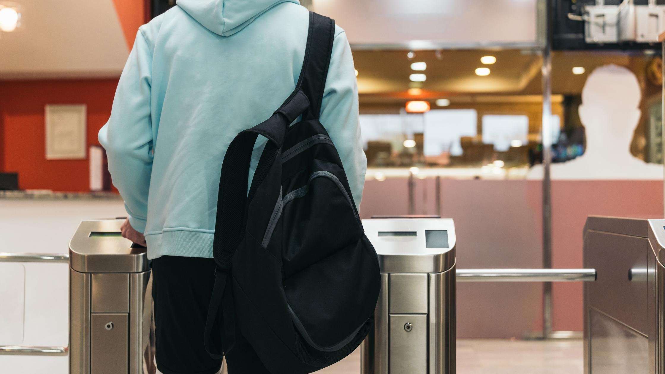 Man with bag walking through turnstiles in a light blue hoodie